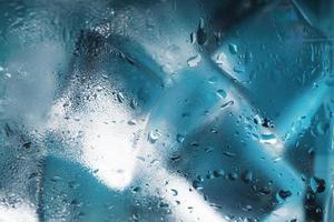 ijs kubussen in een glas met kristal Doorzichtig water Aan een blauw achtergrond. zacht selectief focus foto