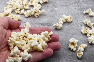 mannetje hand- houdt popcorn Aan grijs beton achtergrond. foto