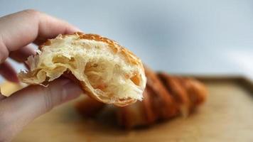 dichtbij omhoog vingers Holding een gescheurd croissant, gouden vers gebakken Frans croissant bakkerij, wazig achtergrond van een ander voor de helft Aan houten dienblad, cafe humeur toon, selectief focus, warm toon foto