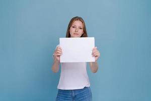 jong vrouw Holding wit papier Aan blauw achtergrond. Kaukasisch vrouw met wit foto