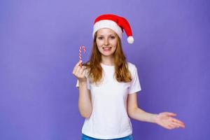 mooi jong meisje in wit t-shirt en de kerstman hoed houdt een feestelijk snoep foto