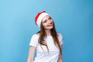 portret van vrouw in de kerstman hoed en wit t-shirt poseren speels Aan blauw foto