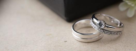 wit goud bruiloft ring met een vogel laser Aan de ring oppervlak. met een zwart ring doos achtergrond en kunstmatig bloemen. Aan de links Daar is een leeg ruimte naar vullen in tekst foto