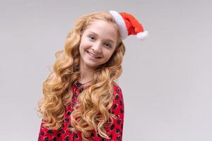 portret mooi meisje in rood de kerstman hoed en jurk met lang golvend haar- looks foto