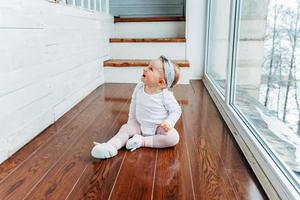 weinig kruipen baby meisje een jaar oud locatie Aan verdieping in helder licht leven kamer in de buurt venster glimlachen en lachend foto