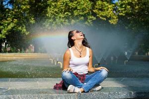 Kaukasisch jong vrouw zittend door fontein geniet koelte van water Aan zonnig foto