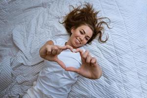 gelukkig jong vrouw wakker worden omhoog in comfortabel wit bed foto