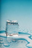 ijs kubus met water druppels Aan een blauw achtergrond. de ijs is smeltend. foto