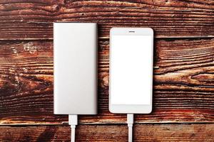 powerbank kosten een smartphone Aan een houten achtergrond. universeel extern accu voor gadgets vrij ruimte en minimalistisch samenstelling. foto