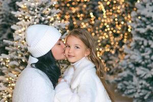 Aziatisch moeder en haar Kaukasisch dochter door de Kerstmis boom buitenshuis. liefde, familie, diversiteit, vakantie concept foto