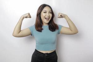 opgewonden Aziatisch vrouw vervelend een blauw t-shirt tonen sterk gebaar door hijs- haar armen en spieren glimlachen trots foto