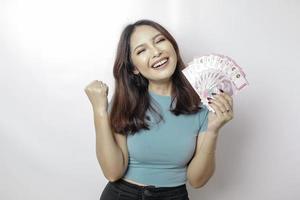 een gelukkig jong vrouw is vervelend blauw t-shirt en Holding contant geld geld in Indonesisch roepia geïsoleerd door wit achtergrond foto