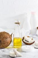 twee types van kokosnoot olie in een pot en een fles en stukken van kokosnoot Aan de tafel. verticaal visie foto