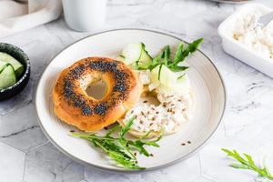 bagel belegd broodje met room kaas, komkommer en rucola Aan een bord Aan de tafel. eigengemaakt ontbijt foto