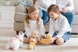 schattig weinig broer en zus zittend Aan verdieping spelen met zacht speelgoed, ouders foto