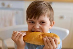 gelukkig knap jong tiener- jongen Holding en aan het eten vers gebakken brood. foto