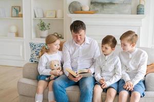 zorgzaam vader leest boek naar zijn weinig dochter en zijn zonen knuffels, zit Aan knus foto