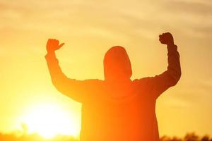 een Mens in de licht van de zonsondergang met zijn handen omhoog, de concept van succes, vrijheid en vreugde foto