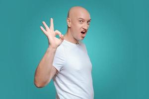 een emotioneel Mens in een wit t-shirt shows met een hand- gebaar dat alles is koel, Aan een titiaan achtergrond foto