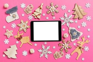 top visie van digitaal tablet Aan roze achtergrond gemaakt van vakantie decoraties en speelgoed. Kerstmis ornament concept foto