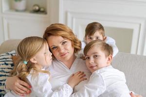 wij liefde jij. glimlachen jong vrouw, kinderen knuffel mam terwijl zittend Aan sofa in leven foto