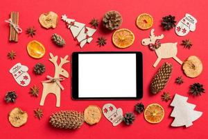 top visie van digitaal tablet, rood achtergrond versierd met feestelijk speelgoed en Kerstmis symbolen rendieren en nieuw jaar bomen. vakantie concept foto