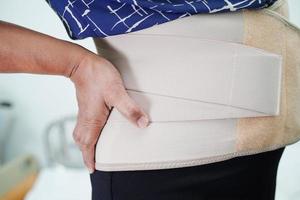 Aziatische senior die een elastische steunriem draagt, kan rugpijn helpen verminderen. foto