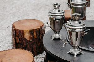 traditioneel theedrinkconcept. drie oude metalen koperen samovars buiten in de buurt van houten stronken. rustieke stijl. foto