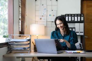 jonge Aziatische zakenvrouw werkt op tablet met laptop op kantoor. foto