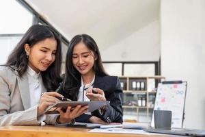 twee jonge aziatische zakenvrouwen bespreken met de presentatie van een nieuw startup-projectidee, analyseren planning en financiële statistieken en investeringsmarkt op kantoor. foto