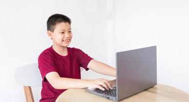 Aziatisch jongen aan het studeren online Aan computer laptop met glimlachen en gelukkig gezicht Bij huis. online onderwijs en e-learning concept. foto