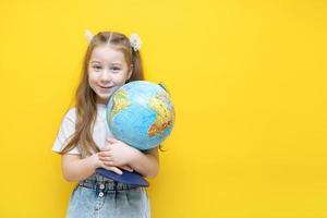 weinig meisje Aan een geel achtergrond knuffels een wereldbol met emoties overweldigend haar foto