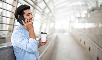 de Mens Holding een kop van koffie en gebruik makend van een smartphone en pratend met zijn vriend terwijl hij aan het wachten zijn vriend Bij de luchthaven. foto
