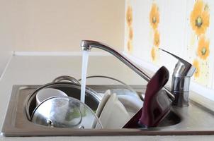 vuil gerechten en ongewassen keuken huishoudelijke apparaten liggen in schuim water onder een kraan van een keuken kraan foto