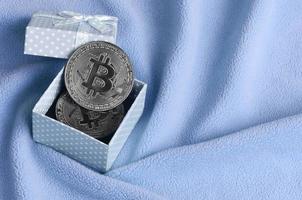 de zilver bitcoin leugens in een klein blauw geschenk doos met een klein boog Aan een deken gemaakt van zacht en pluizig licht blauw fleece kleding stof met een groot aantal van Verlichting vouwen foto