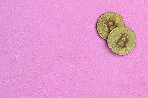 twee gouden bitcoins leugens Aan een deken gemaakt van zacht en pluizig licht roze fleece kleding stof. fysiek visualisatie van virtueel crypto valuta foto