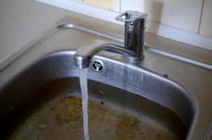 roestvrij staal wastafel plug gat dichtbij omhoog vol van water en deeltjes van voedsel foto