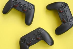 drie modern zwart gamepads Aan geel achtergrond. laten we Speel video spellen samen met vrienden concept. coöperatie teamplay foto