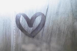 een hartvormig tekening getrokken door een vinger Aan een beneveld glas in regenachtig weer foto