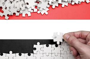 Jemen vlag is afgebeeld Aan een tafel Aan welke de menselijk hand- vouwen een puzzel van wit kleur foto