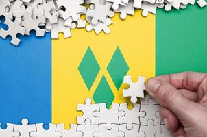 heilige vincent en de grenadines vlag is afgebeeld Aan een tafel Aan welke de menselijk hand- vouwen een puzzel van wit kleur foto