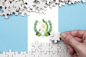 Guatemala vlag is afgebeeld Aan een tafel Aan welke de menselijk hand- vouwen een puzzel van wit kleur foto