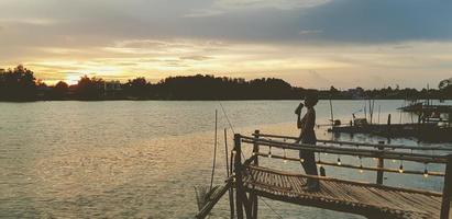 Bangkok, Thailand - juni 29, 2022 silhouet van vrouw staan Aan houten waterkant, waterkant of brug met rive en boom achtergrond Bij zonsondergang of zonneschijn. mooi natuur. natuurlijk behang. foto