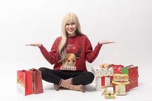 portret van gelukkig Kaukasisch jong vrouw in in Kerstmis trui met geschenk doos en boodschappen doen Tassen over- wit achtergrond foto