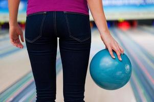 zelfverzekerd speler. achterzijde visie van jong Dames Holding een bowling bal terwijl staand tegen bowling steegjes foto