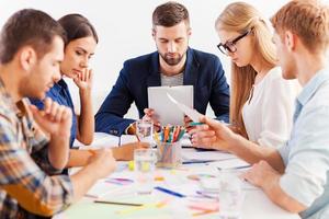 geconcentreerd Aan werk. groep van zelfverzekerd bedrijf mensen in slim gewoontjes slijtage werken samen terwijl zittend Bij de tafel foto