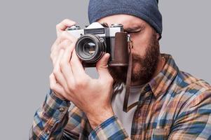 glimlach naar de camera knap jong gebaard Mens fotograferen u met zijn oubollig camera terwijl staand tegen grijs achtergrond foto