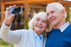 liefde in focus. gelukkig senior paar bonding naar elk andere en maken selfie terwijl staand buitenshuis foto