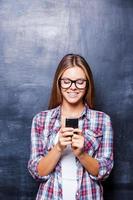 telefoon wieg. vrolijk jong Dames Holding telefoon en glimlachen terwijl staand tegen schoolbord foto