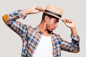 in de ritme van mijn leven. knap jong Afro Amerikaan hipster Holding handen Aan zijn hoed terwijl staand tegen grijs achtergrond foto